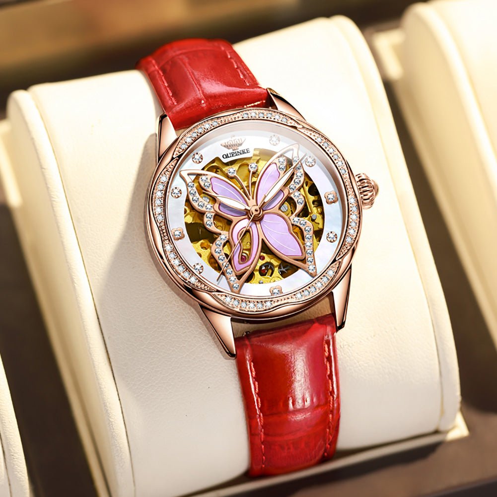 Watch with red strap and butterfly design on a white cushion